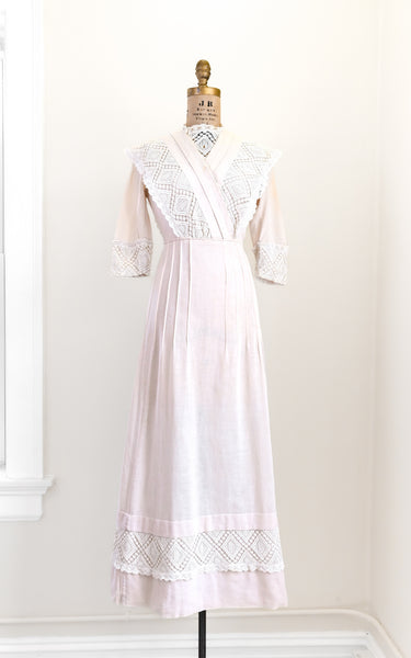 Pink dress with white lace details on a mannequin against a white wall.